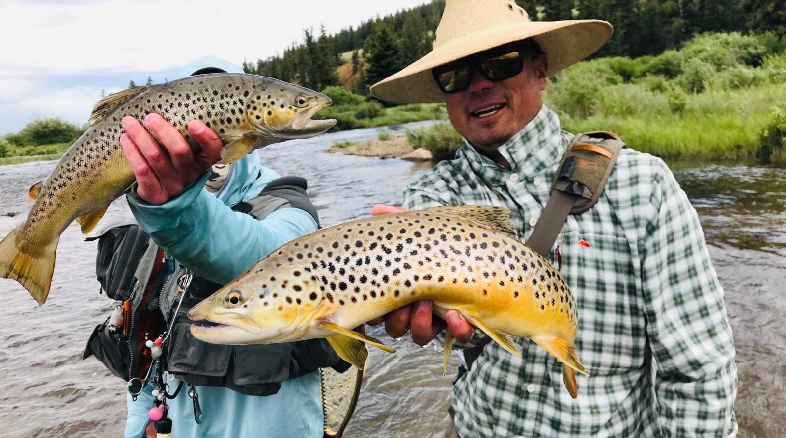 Two men holding brown trout while standing in a river